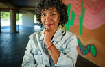 A woman smiles to camera, standing in front of a wall painted with a mural of cactuses