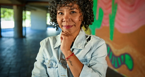 A woman smiles to camera, standing in front of a wall painted with a mural of cactuses