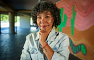 A woman smiles to camera, standing in front of a wall painted with a mural of cactuses