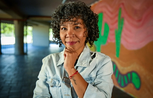 A woman smiles to camera, standing in front of a wall painted with a mural of cactuses