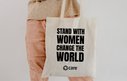 A person holding a tote bag with the slogan 'Stand with women change the world'