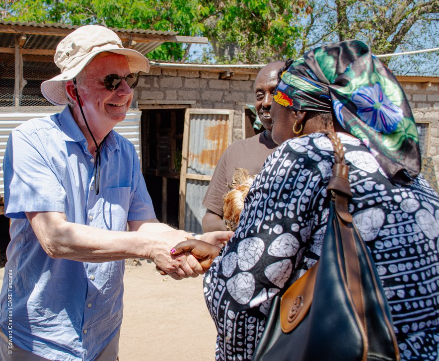 An older man shakes hands with a woman who is carrying a chicken