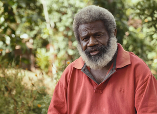 A man with a large white beard in front of some greenery