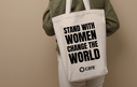 A person holding a tote bag with the slogan 'Stand with Women Change the World' plus the CARE logo