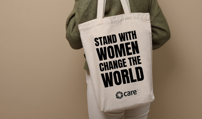 A person holding a tote bag with the slogan 'Stand with Women Change the World' plus the CARE logo