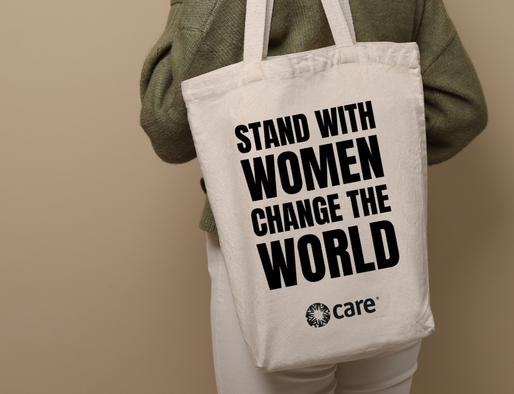 A person holding a tote bag with the slogan 'Stand with Women Change the World' plus the CARE logo