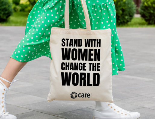 A person in a green polka dot skirt carries a tote bag with the slogan 'STAND WITH WOMEN CHANGE THE WORLD' and the CARE logo