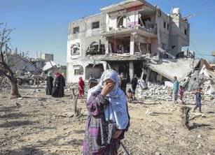 A woman looking very distressed in front of a building damaged by bombing