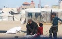 A woman sits with two children outside a tent with her hand to her head in despair