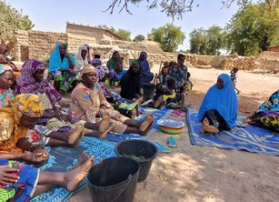 A group of around 20 women sit together outdoors holding a discussion