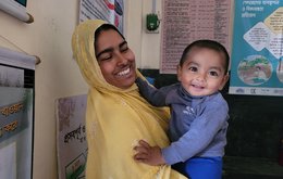 A baby/young toddler in his mother's arms, both smiling