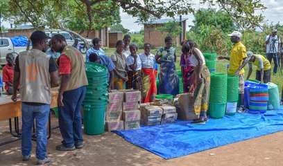 Several people stand in line in front of emergency supplies for distribution