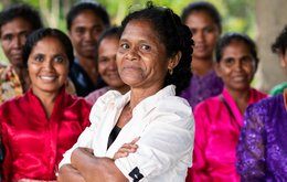 A woman stands confidently with her arms folded in front of a group of women