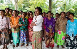 A group of about 20 women stand with their arms folded looking to camera; a woman in a white shirt stands in the foreground