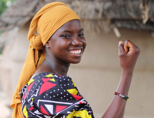 A woman smiles to the camera with her arm raised and fist clenched in an empowering manner