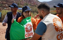 A man wearing a cARE jacket hands a green CARE package to a woman