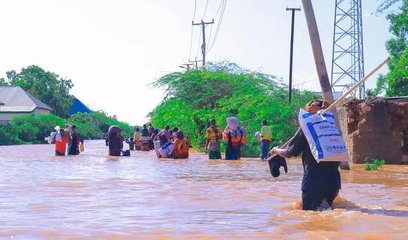 A group of people risking their lives travelling across a flooded road whilst holding possessions above their heads.