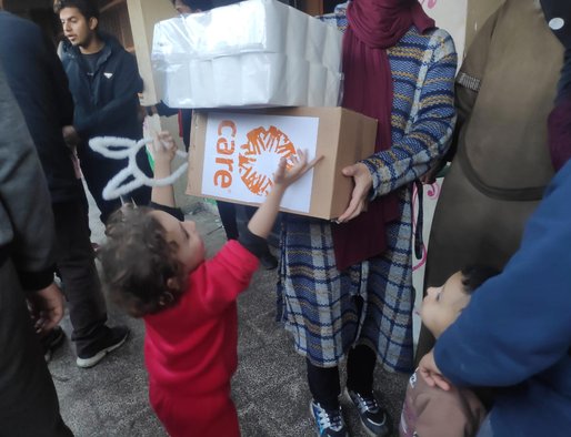 A young children reaches up towards a cardboard box with a CARE logo on it