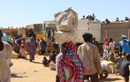 A large group of refugees load luggage onto trucks