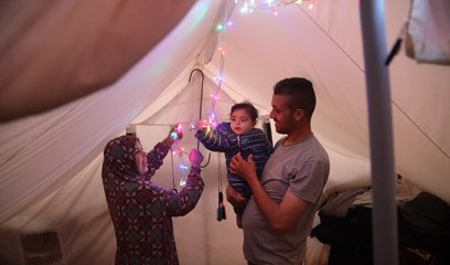 A woman, man and baby in a tent - the woman is hanging up fairy lights