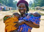 A woman smiles broadly holding two babies wrapped in colourful clothing