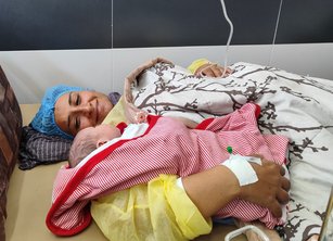 A woman lies on a hospital bed with a new born baby, with a contented smile on her face