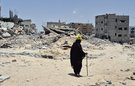 A person dressed all in black walks with a stick amid the rubble of destroyed buildings