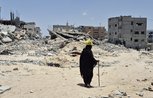 A person dressed all in black walks with a stick amid the rubble of destroyed buildings