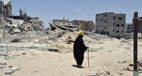 A person dressed all in black walks with a stick amid the rubble of destroyed buildings