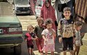 A mother and five children walking down a dusty road together