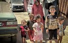 A mother and five children walking down a dusty road together