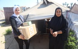 Two women standing in front of a tent, one of them is holding a cardboard box with the CARE logo on it