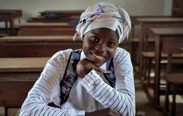 A girl sits smiling at a desk in an empty classroom