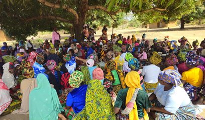 A large group of women gather together in a meeting under a tree
