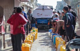 People queue up with water cans behind a truck carrying water