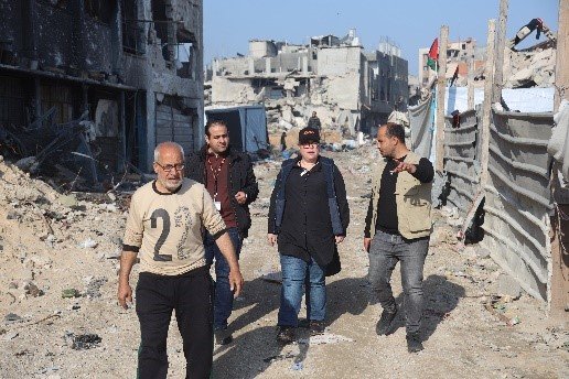 Four people walk among the rubble of destroyed buildings