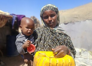 A woman carries a small boy and a bright yellow water container