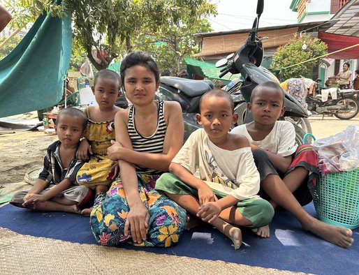 A mother and four children sit on a mat on the floor