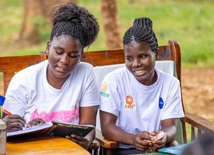 Two women sit on a bench looking at paperwork together