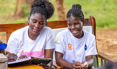 Two women sit on a bench looking at paperwork together