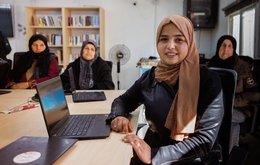 A group of four women sit around desks at computers