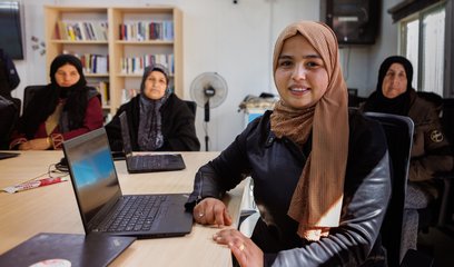 A group of four women sit around desks at computers