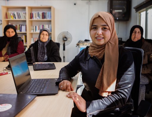 A group of four women sit around desks at computers