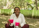 A young woman holds two bright pink purses which likely contain sanitary products