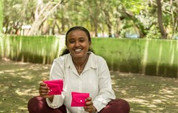 A young woman holds two bright pink purses which likely contain sanitary products