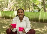 A young woman holds two bright pink purses which likely contain sanitary products
