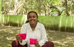 A young woman holds two bright pink purses which likely contain sanitary products
