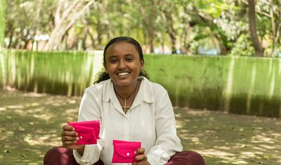 A young woman holds two bright pink purses which likely contain sanitary products