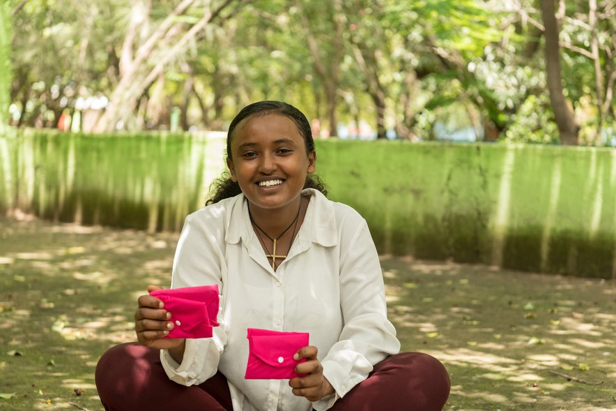 A young woman holds two bright pink purses which likely contain sanitary products
