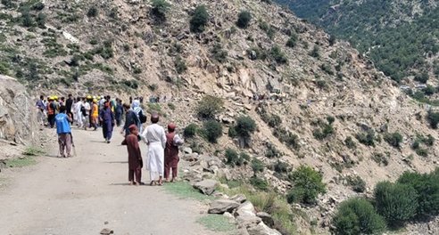 A group of people walking along a road cutting through mountains